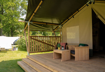 Überdachte Terrasse mit Holzmöbeln vor einem Safarizelt mit Sanitär am Jocomo Parc in Belgien.