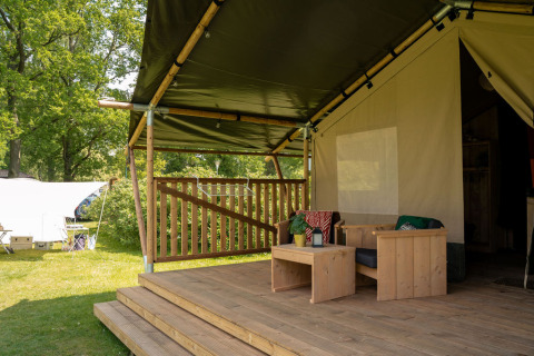 Terrasse en bois couverte avec salon devant une tente safari avec sanitaires au Jocomo Parc, Belgique.