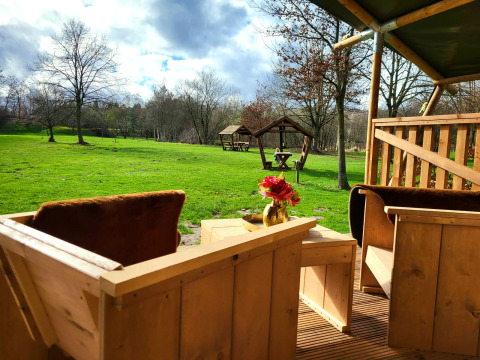 Vista desde la terraza de madera de una tienda safari con sanitarios en Jocomo Parc, Bélgica, campo verde.