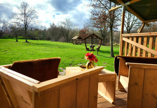 Vista desde la terraza de madera de una tienda safari con sanitarios en Jocomo Parc, Bélgica, campo verde.