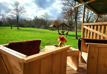 Vista desde la terraza de madera de una tienda safari con sanitarios en Jocomo Parc, Bélgica, campo verde.