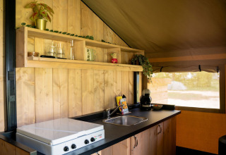 Cocina en tienda safari con paredes de madera, estufa, fregadero y estantes en Jocomo Parc, Bélgica.