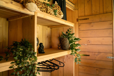 Cozy wooden closet in a safari tent at Jocomo Parc, Belgium, decorated with plants and a plush leopard.