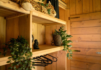 Cozy wooden closet in a safari tent at Jocomo Parc, Belgium, decorated with plants and a plush leopard.