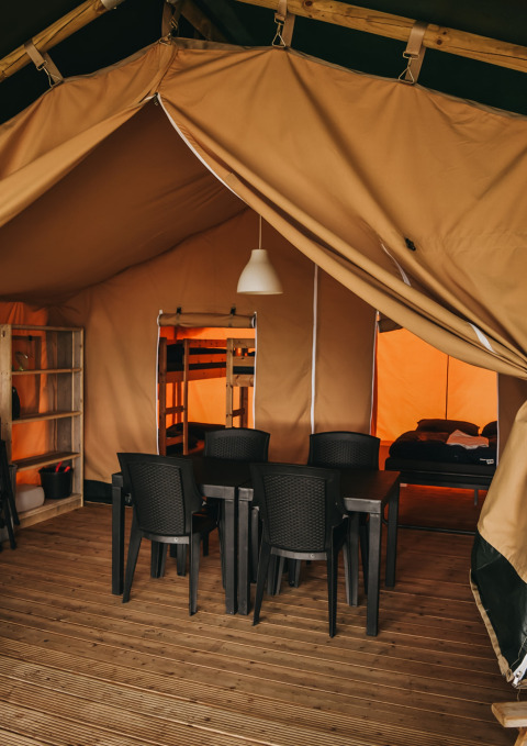 Innenraum des Safari-Zelts im Camping Lucherino, Italien, mit Esstisch, Stühlen und Schlafbereich.