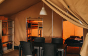 Innenraum des Safari-Zelts im Camping Lucherino, Italien, mit Esstisch, Stühlen und Schlafbereich.