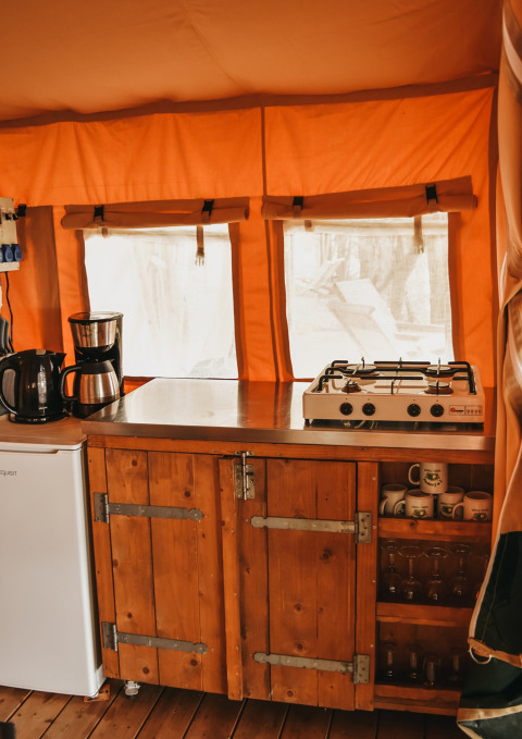 Coin cuisine sous tente Safari Valley au Camping Lucherino en Italie, frigo, plaques gaz et meubles en bois.