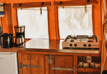 Coin cuisine sous tente Safari Valley au Camping Lucherino en Italie, frigo, plaques gaz et meubles en bois.