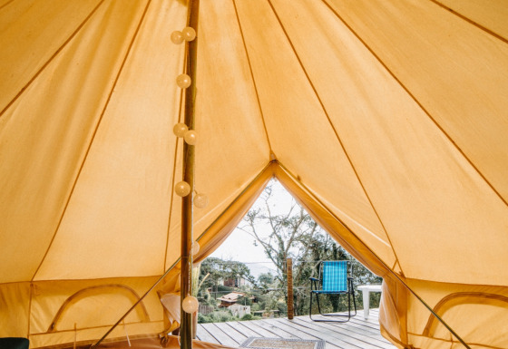 Vue intérieure d'une tente safari Belltent, montrant un lit, guirlande lumineuse et terrasse avec chaise.