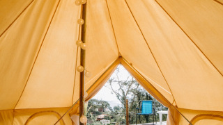 Vue intérieure d'une tente safari Belltent, montrant un lit, guirlande lumineuse et terrasse avec chaise.