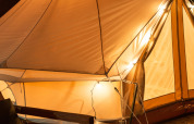 Tente safari éclairée Belltent au Camping Lucherino en Italie, sur terrasse en bois et fauteuil confortable la nuit.