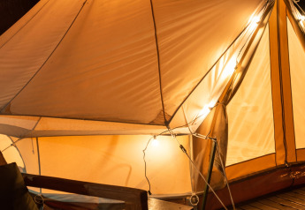 Tente safari éclairée Belltent au Camping Lucherino en Italie, sur terrasse en bois et fauteuil confortable la nuit.