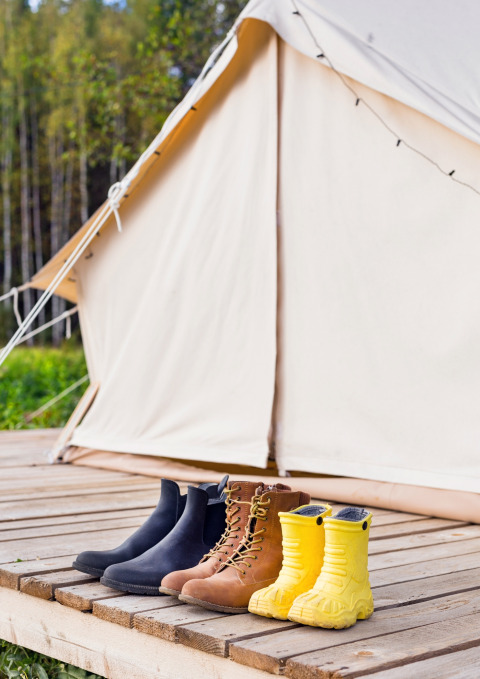 Botas y botas de agua afuera de una tienda Belltent en Camping Lucherino, Italia, con bosque al fondo.