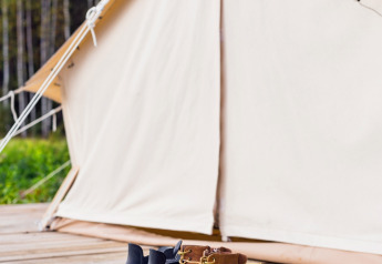 Bottes alignées devant une tente Belltent au Camping Lucherino en Italie, forêt visible en arrière-plan.