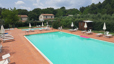 Piscina all'aperto con lettini e ombrelloni al Camping Monti del Sole, parco vacanze in Umbria, Italia.