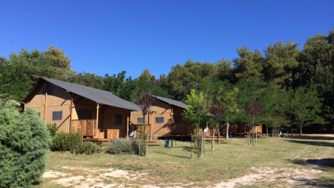 Due tende safari al Camping Monti del Sole in Umbria, Italia, circondate da alberi e cielo azzurro.