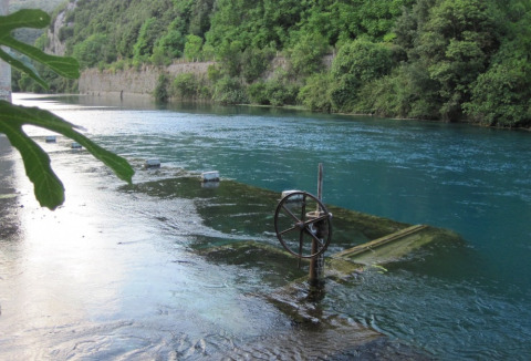 River with submerged platform and handwheel at Camping Monti del Sole, Umbria, Italy, surrounded by forest.