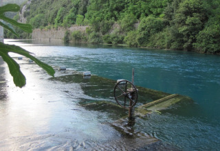 Fiume con piattaforma sommersa e volantino al Camping Monti del Sole, Umbria, Italia, circondato da boschi.