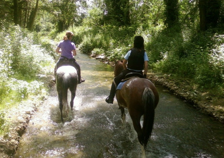 Twee mensen rijden te paard door een bosbeekje bij Camping Monti del Sole, een vakantiepark in Umbrië, Italië.