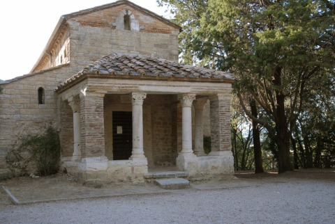 A historic stone chapel with columns at Camping Monti del Sole, Umbria, Italy, surrounded by trees.