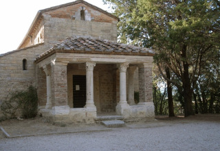 A historic stone chapel with columns at Camping Monti del Sole, Umbria, Italy, surrounded by trees.