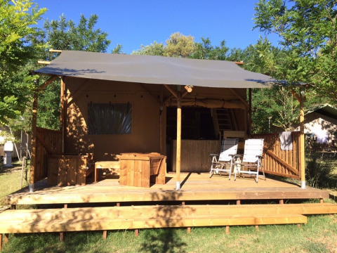 Træhytte med overdækket terrasse og loungestole på Camping Monti del Sole i Umbrien, Italien på en solrig dag.