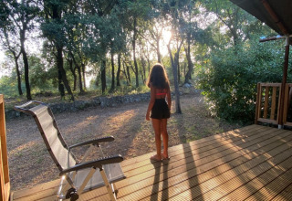 Person standing on a wooden terrace in forest sunlight at Camping Monti del Sole holiday park in Umbria, Italy.