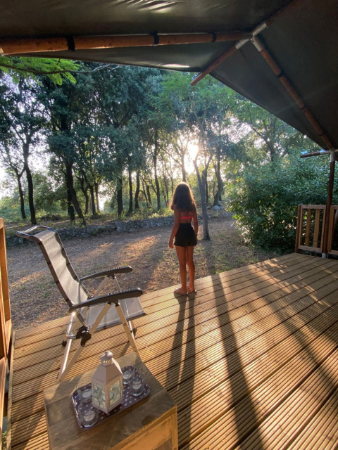 Person standing on a wooden terrace in forest sunlight at Camping Monti del Sole holiday park in Umbria, Italy.