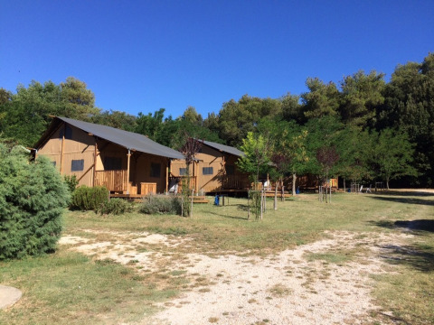 Camping Monti del Sole in Umbria, Italy, featuring glamping tents, grassy fields, trees, and clear blue sky.