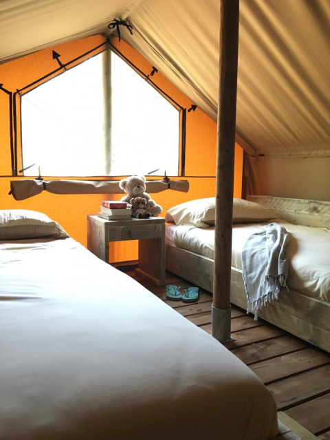 Two single beds inside a cozy tent at Camping Monti del Sole, with books and teddy bears on a nightstand.