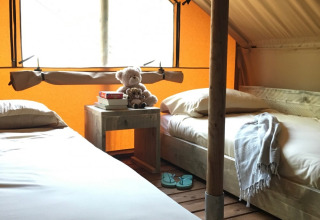 Two single beds inside a cozy tent at Camping Monti del Sole, with books and teddy bears on a nightstand.