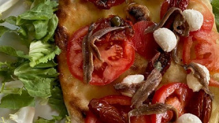 Pizza au pain plat italien garnie de tomates, mozzarella, anchois et salade, servie sur une assiette blanche.