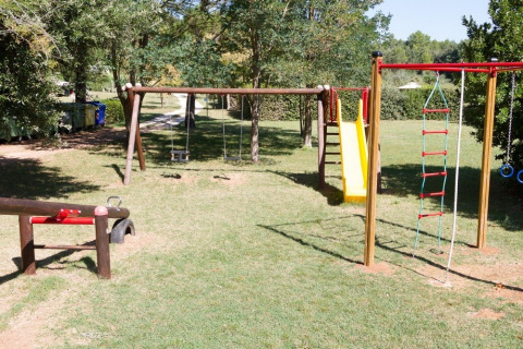 Playground at Camping Monti del Sole in Umbria, Italy, with swings, slide, and climbing ladder on grass.