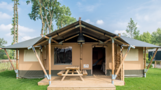 Tenda safari Medley Lodge con veranda coperta, tavolo da picnic e prato verde ben curato.