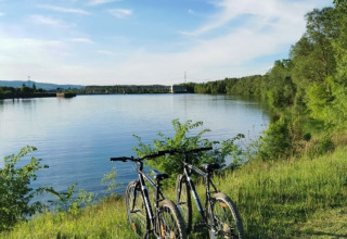Dos bicicletas junto al lago en Camping de Thoissey, un parque vacacional en Auvergne-Rhône-Alpes, Francia, con cielo azul.