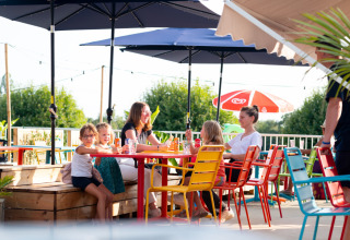 Gezin aan kleurrijke tafels op het terras bij Camping de Thoissey in Auvergne-Rhône-Alpes, Frankrijk.