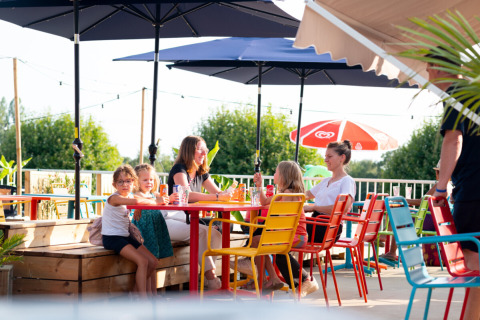 Family enjoying drinks at colorful outdoor seating at Camping de Thoissey, Auvergne-Rhône-Alpes, France.