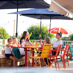 Familie nyder solrigt udendørsområde med farverige stole på Camping de Thoissey i Auvergne-Rhône-Alpes.