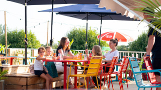 Familie nyder solrigt udendørsområde med farverige stole på Camping de Thoissey i Auvergne-Rhône-Alpes.