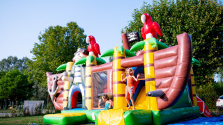 Børn leger på en oppustelig piratskibs-hoppeborg i solen på Camping de Thoissey i Auvergne-Rhône-Alpes.