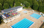 Luftfoto af Camping de Thoissey med poolområde, rutsjebane, restaurant og skov i baggrunden.