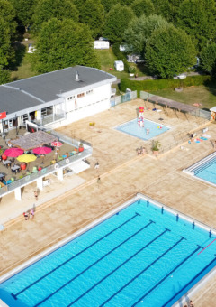 Luftfoto af Camping de Thoissey med poolområde, rutsjebane, restaurant og skov i baggrunden.