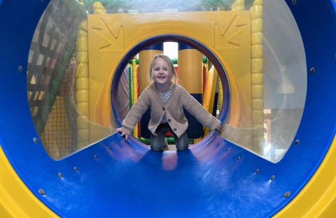Ein lächelndes Kind krabbelt durch einen bunten Tunnel im Ferienpark Den Blanken in Gelderland.