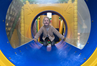 Een kind speelt in een kleurrijke tunnel op de indoor speelplaats van Recreatiepark Den Blanken, Gelderland.