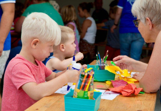 Kinderen en een volwassene knutselen samen aan een tafel in Recreatiepark Den Blanken, Gelderland.