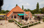 Udendørs caféområde ved feriepark Den Blanken i Gelderland, Holland, med terrasse, borde og parasoller.