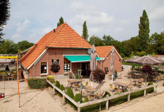 Udendørs caféområde ved feriepark Den Blanken i Gelderland, Holland, med terrasse, borde og parasoller.