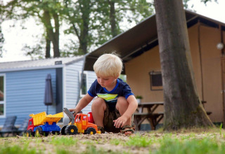 Young boy playing with toy trucks in the sand outside cabins at Recreation Park Den Blanken, Gelderland.