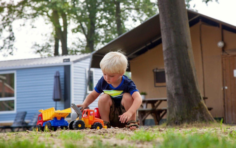 Jonge jongen speelt met speelgoedvrachtwagens in het zand bij huisjes op Recreatiepark Den Blanken.