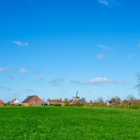 Campo cerca de Neede en Gelderland, Países Bajos, con verdes prados, casas y un molino de viento.